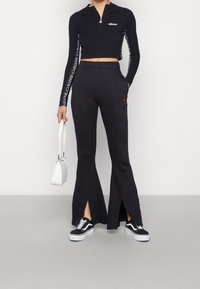 Svart kort zip-up topp med logotyp, kombinerad med svarta flared byxor med sidofyssningar, samt svartvita sneakers. Vit väska.