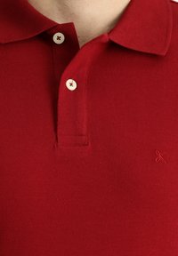 Polo rosso realizzato in cotone testurizzato, con colletto classico, placket a tre bottoni e logo cucito con filo rosso abbinato.