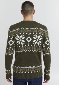 Pulover tricotat de culoare verde măslin, cu modele albe de fulgi de zăpadă și diamante, având manșete și tiv cu nervuri. Material texturat, cu un aspect cald.