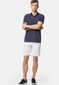 Granatowa i biała koszulka polo w paski z krótkim rękawem, zestawiona z białymi szortami i ciemnymi sneakersami, o luźnym kroju i klasycznym designie.