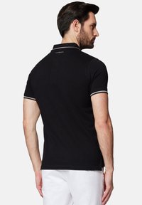 Czarna koszulka polo z krótkimi rękawami, o jednolitym designie, z kontrastowymi paskami na mankietach. Na plecach, na dekolcie, znajduje się logo.