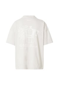 Hvid oversized T-shirt med et bagdesign, der viser en moka-kande, blomster og sætningen "the little things."