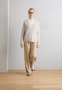 Pull en laine beige, chemise à col blanc en dessous, pantalon beige et chaussures grises avec des accents clairs. Textures lisses, coupe décontractée.