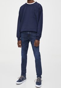 Marinblå sweatshirt med vit krage, framficka; matchad med mörkblå jeans och marinblå sneakers med grå snören. Enkla och avslappnade design.