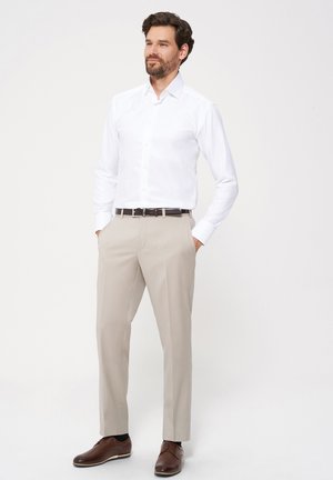 Camisa blanca de manga larga con botones en la parte delantera, pantalones beige, zapatos de cuero marrón y un cinturón marrón oscuro. Textura de tela suave en toda la prenda.