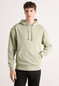 Sudadera de algodón verde claro con un bolsillo frontal, cordones ajustables y puños de canalé. Logo exhibido en el pecho.