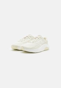 Pár béžovo-bílých lehkých síťovaných tenisek s tlustými polstrovanými podrážkami položených vedle sebe na bílém pozadí.