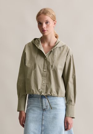 Geknipte hoodie in olijfgroen met een wit geruit patroon, voorzien van knoopsluiting en een trekkoord in de taille, gecombineerd met een denimrok.