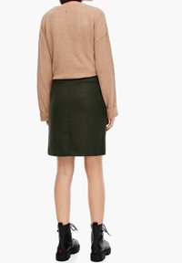 Pull beige avec des manches texturées, associé à une jupe droite vert foncé. Bottines noires avec une semelle épaisse et des lacets.