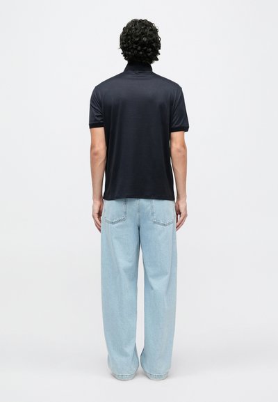 Tumši zils polo krekls ar vienkāršu dizainu un īsām piedurknēm, kombinēts ar gaiši zilām platām džinsa biksēm. Gluda auduma tekstūra, minimālas detaļas.