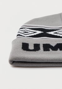 Gorro de malha cinza dobrado com padrão geométrico preto e branco e letras pretas em destaque na borda, contra um fundo branco liso.