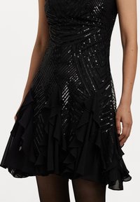 Μαύρο φόρεμα με εφαρμοστό μπούστο διακοσμημένο με παγιέτες και ντραπέ τελείωμα. Το υλικό είναι λείο με γυαλάδα.