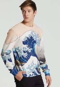 Camisa de manga larga con un diseño de olas en azul y blanco sobre un fondo melocotón, con patrones contrastantes y un corte relajado.