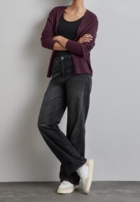 Czarne szerokie dżinsy zestawione z bordowym kardiganem na czarnej bluzce. Sneakersy mają białe i szare detale. Gładka tekstura, casualowy design.