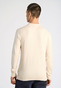 Vaaleanbeige neulepaita, jossa on pitkät hihat, resorit hihansuissa ja helmassa sekä klassinen kaulus. Pehmeä rakenne, vartalonmyötäinen siluetti, minimalistinen muotoilu.
