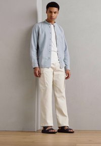 Svjetloplavi košuljasti sako, bijela majica, kremaste kordura cargo hlače i crne sandale. Jednostavan dizajn s kontrastnim teksturama.