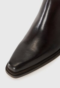Bota de cuero negro con un acabado pulido, punta afilada y un sutil tacón apilado. Presenta un diseño limpio y una textura suave.