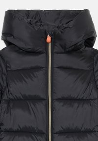 Zwarte, gevoerde jas met een hoge kraag en capuchon. Voorzien van een voorgeroerde rits met een gouden tint en een oranje trekband. Glad, glanzend oppervlak.