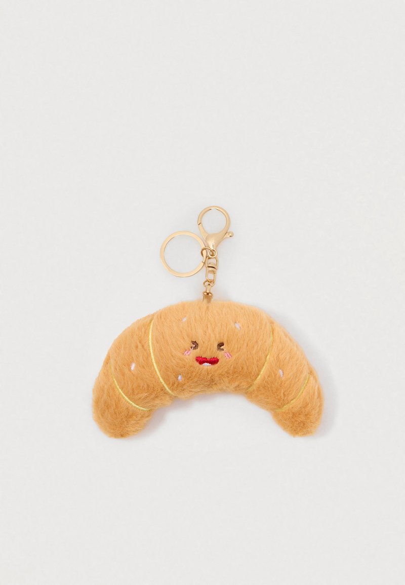 Porte-clé en forme de croissant moelleux avec un visage souriant brodé et un anneau et un fermoir en or sur un fond blanc.