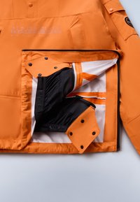 Orange Napapijri jakke med delvist åbnet front, der viser sort inderside og knaplukninger på en hvid baggrund.