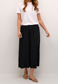 Svart, flödande ankellång kjol i lättviktsmaterial med elastisk midja, kombinerad med en enkel vit t-shirt och beige ballerina. 