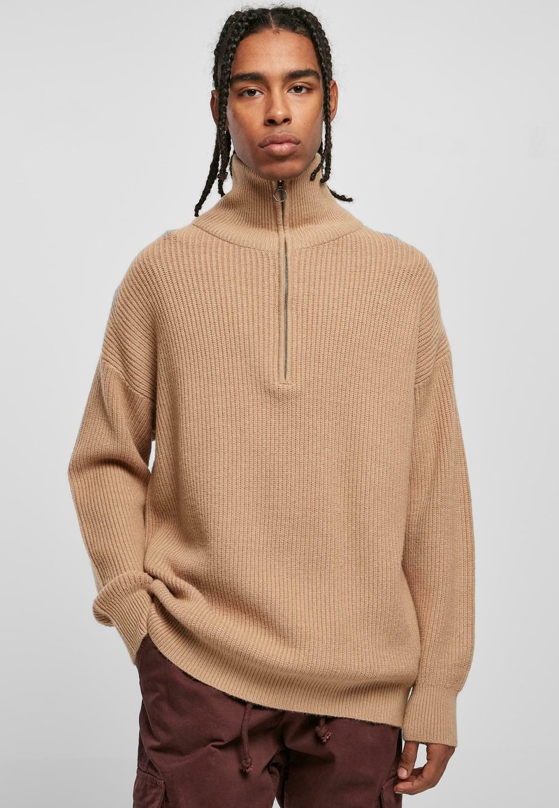 Beige ribbestrikket genser med høy krage og glidelås foran. Oversized passform med senkede skuldre og lange ermer. Teksturert strikket stoff.