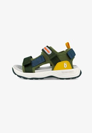 Sandalia abierta para niños con tiras de tela verdes, detalles en azul y amarillo, suela blanca y cierres ajustables de velcro.
