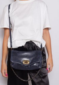 Borsa a tracolla in pelle blu navy con design a patta, chiusura in hardware dorato e tracolla a catena. Texture liscia e aspetto minimalista.