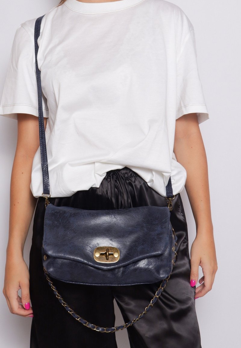 Borsa a tracolla in pelle blu navy con design a patta, chiusura in hardware dorato e tracolla a catena. Texture liscia e aspetto minimalista.