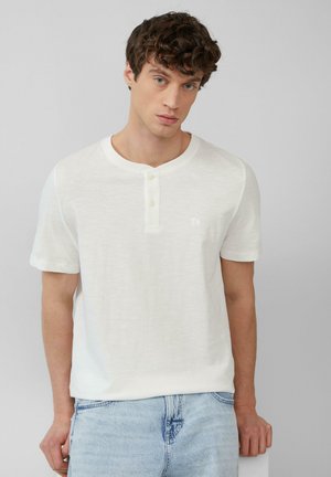 Witte korte mouwen henley-shirt met een ronde hals en een placket met drie knopen. Zachte textuur met een subtiel logo op de borst. G gedragen met lichte spijkerbroek.