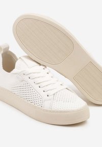 Des baskets blanches en mesh présentent un design à lacets, des panneaux latéraux texturés, une tige lisse et une semelle en caoutchouc avec un motif de semelle ondulée.