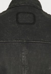 Czarna skórzana kurtka o fakturowanym wykończeniu, z kwadratowym haftowanym wzorem na plecach. Szwy podkreślone widocznym przeszyciem.