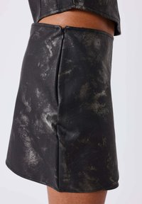 Jupe en simili cuir noir avec une finition brillante et texturée. Elle présente une fermeture éclair latérale visible et une forme A-line simple.