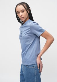 Tricou albastru cu mâneci scurte, confecționat dintr-un material moale, cu un logo brodat subtil pe piept și un design clasic cu guler rotund.