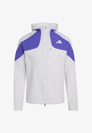 Bílá bunda s kapucí na zip vpředu, fialové panely na ramenech a horních pažích a malé bílé logo na levé straně hrudi.