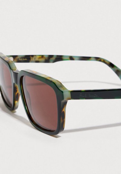 Γυαλιά ηλίου με σχέδιο ζώου χελώνας, με πράσινο και καφέ σκελετό, καφέ φακούς και τετράγωνο σχήμα. Διαθέτουν λογότυπο στο πλαϊνό μέρος του σκελετού.