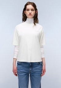 Witte katoenen T-shirt met een hoge hals, korte mouwen en een klein logo op de borst. Draag het over een lange mouwen top en combineer het met blauwe jeans.