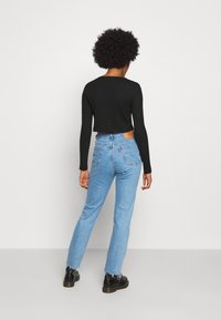 Svart ribbad långärmad croptop i kombination med ljusblå högmidjade jeans som har en blekt tvätt och en brun läderlapp på baksidan.
