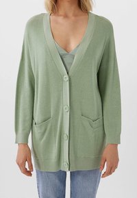 Cardigan verde chiaro realizzato in un materiale a maglia testurizzato, con scollo a V profondo, bottoni frontali e due tasche frontali.