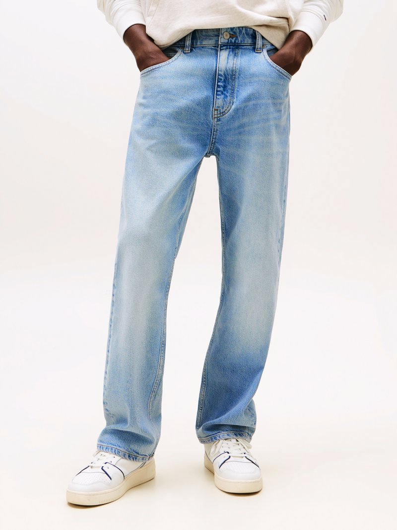 Jeans in denim azzurro chiaro con vestibilità a gamba dritta, dotati di tasche frontali e chiusura a bottone. Indossati con sneakers bianche.