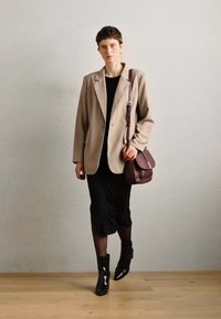 Blazer beige sur une robe noire, associé à des bottines noires et un sac à bandoulière bordeaux. Tissu lisse, design structuré et silhouette ajustée.