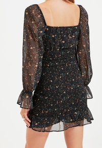 Black floral dress with sheer bell sleeves, smocked bodice, and ruffled hem. Features multicolored flower patterns against a dark background.