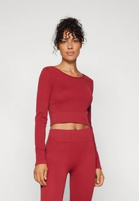 Piros bordázott, hosszú ujjú, kerek nyakú rövid felső, amelyhez illő magas derekú leggings párosul. Puha, rugalmas anyag.