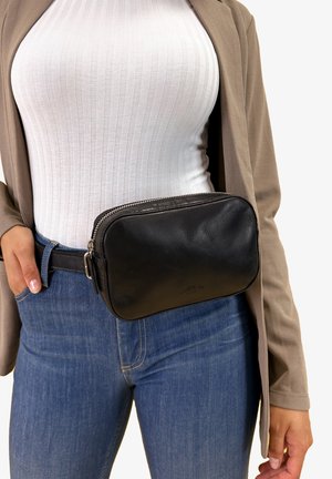 Black leather belt bag with a zip closure, rectangular shape, textured surface, and metal hardware, worn on a waist with blue jeans.