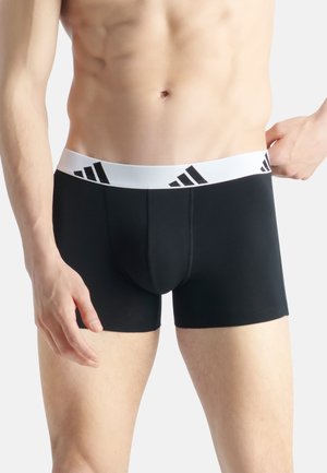 Boxers noirs en tissu extensible, dotés d'une ceinture blanche avec un logo de marque noir. Texture lisse et coupe ajustée.