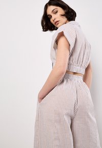 Conjunto de dos piezas que incluye una blusa corta con cuello y pantalones de pierna ancha, fabricados en una tela ligera con finas rayas beige y blancas.