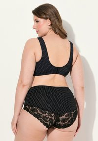 Sostenedor negro con lunares, con tirantes anchos y cierre en la parte posterior, combinado con pantalones cortos negros con un borde de encaje floral y una textura de tela suave.