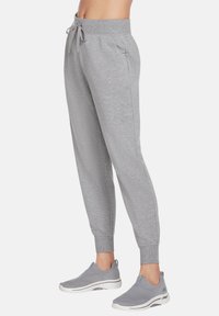 Gray jogger pants made of soft fabric, featuring an elastic waistband with a drawstring, side pockets, and tapered ankles. Paired with gray sneakers.