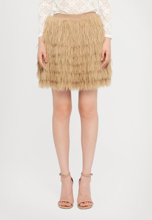 Beige faux karusnahast mini seelik, millel on tekstureeritud ja kihiline disain. Kombineeritud nude värvi jalatallaga kontsakingadega, esitatud valge taustaga.