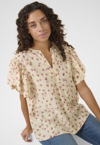 Blumige Bluse in Hellgelb mit Puffärmeln, verziert mit pinken und lila Mustern. Der Stoff hat eine strukturierte Oberfläche und einen V-Ausschnitt.